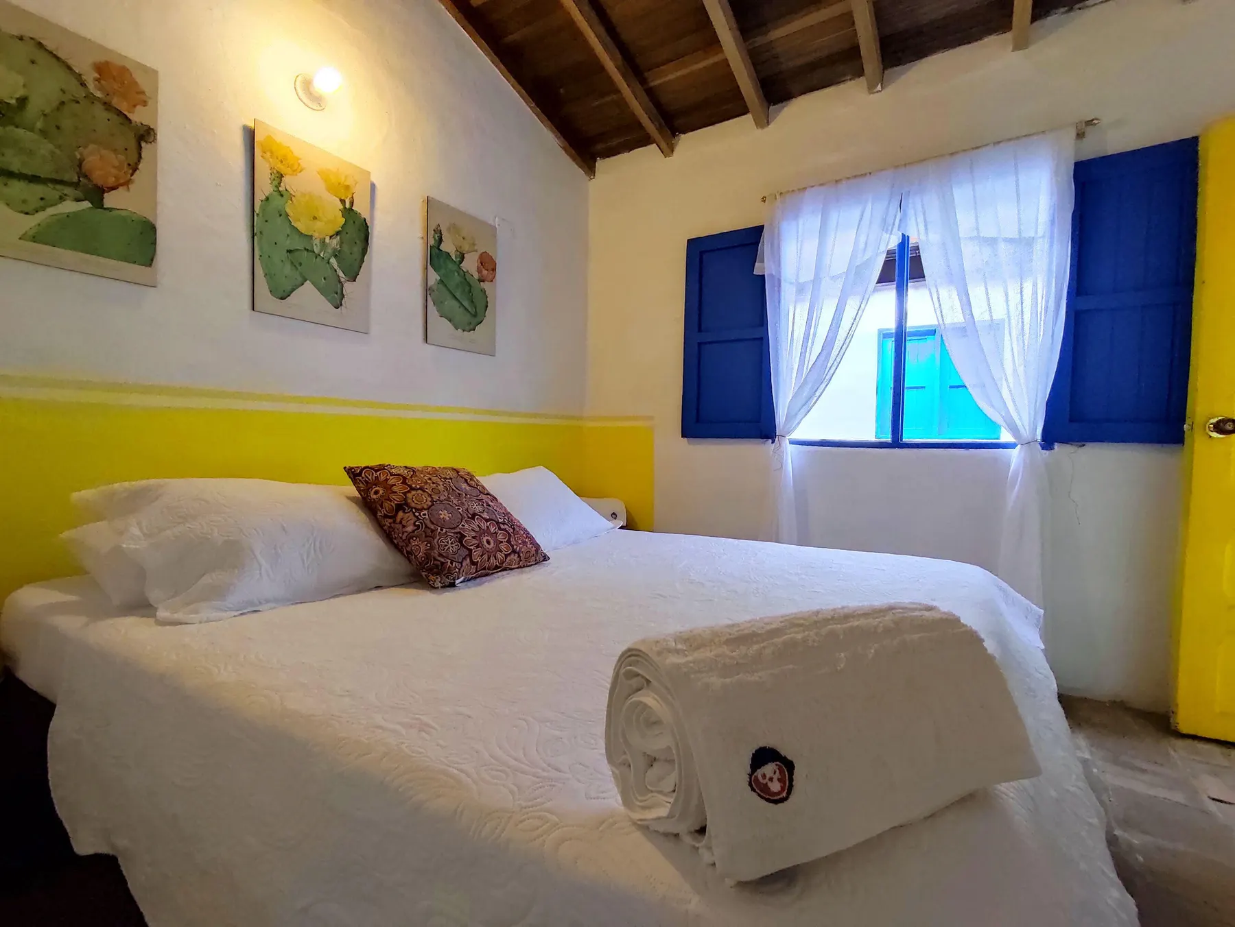 Habitación Doble de Trip Monkey Barichara con cuadros de cactus y ventana azul
